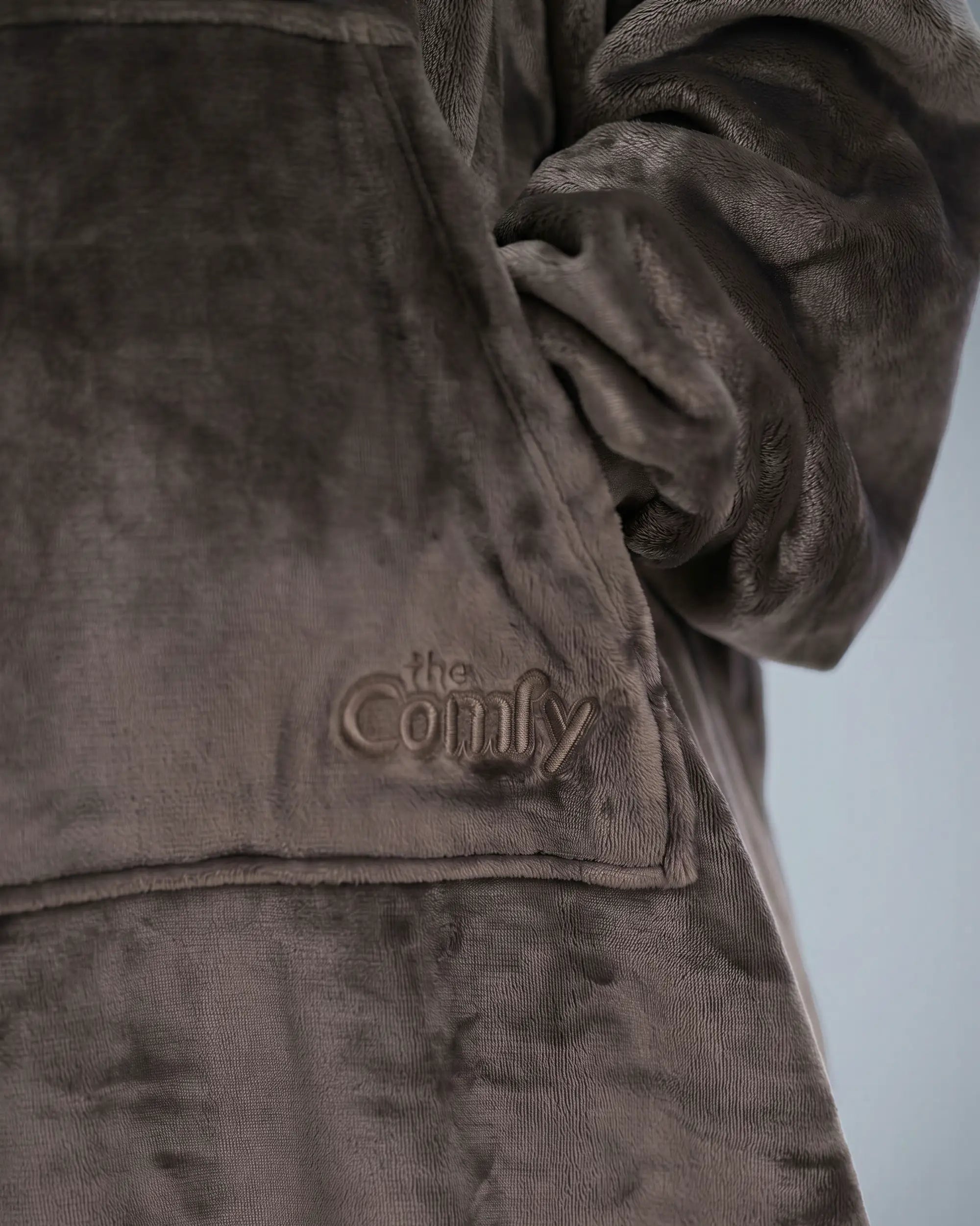 Close-up detail of The Dream Long fabric featuring the ultra-soft microfiber texture, kangaroo pocket construction, and tonal embroidered The Comfy logo.
