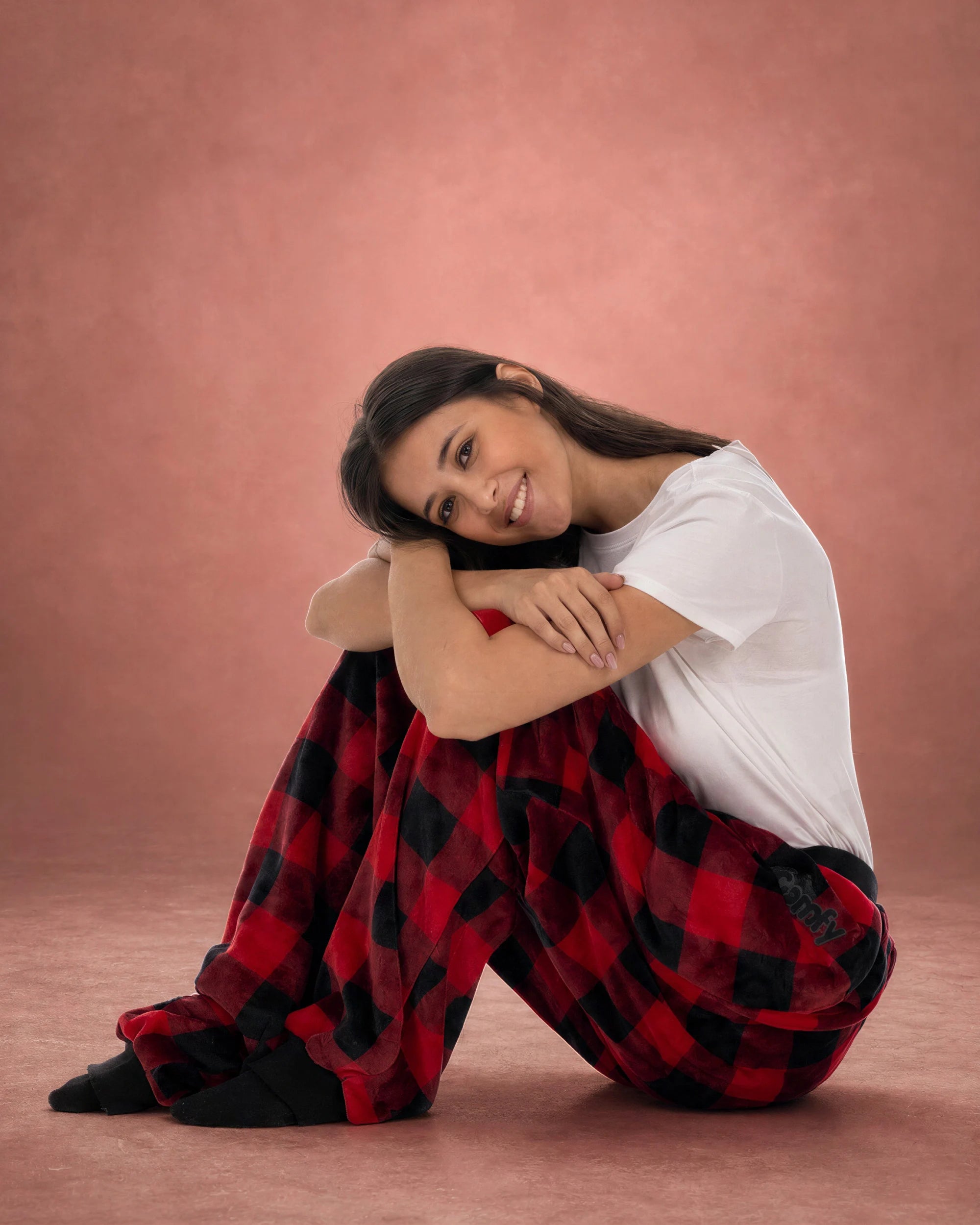 Woman sitting with knees hugged while wearing Dream Pants in Red Plaid, showcasing the cozy fit and soft plaid fabric.