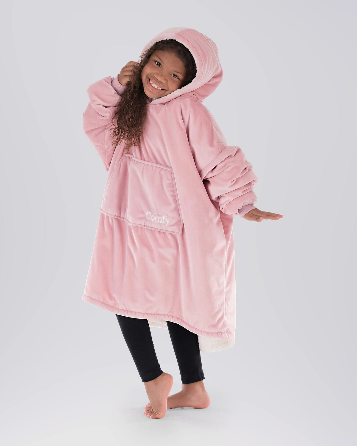 Child wearing The Original Jr. Blush wearable blanket in a playful pose, highlighting the oversized fit and soft hood.