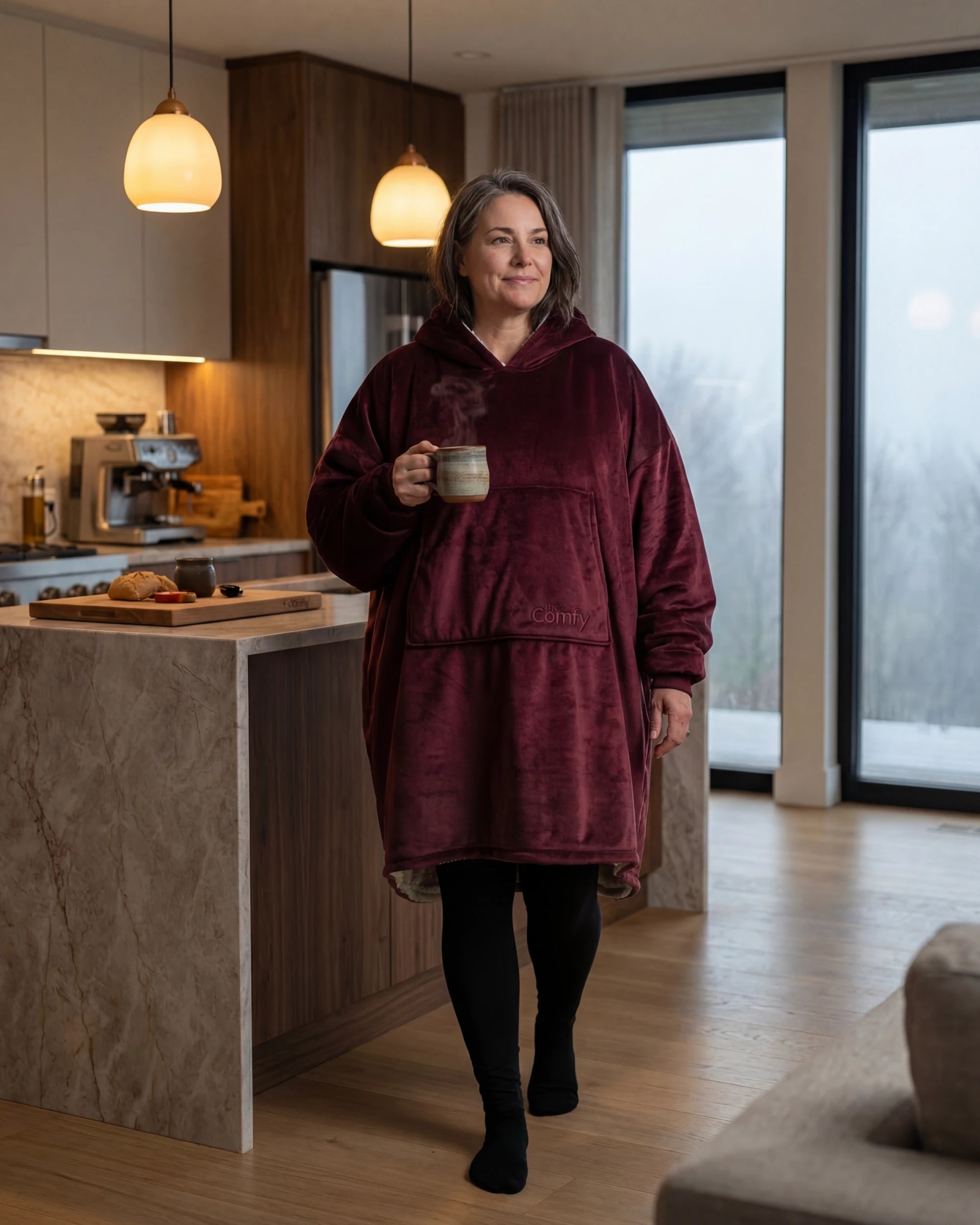 Front view of woman walking through kitchen showing front view of Original wearable blanket hoodie in burgundy