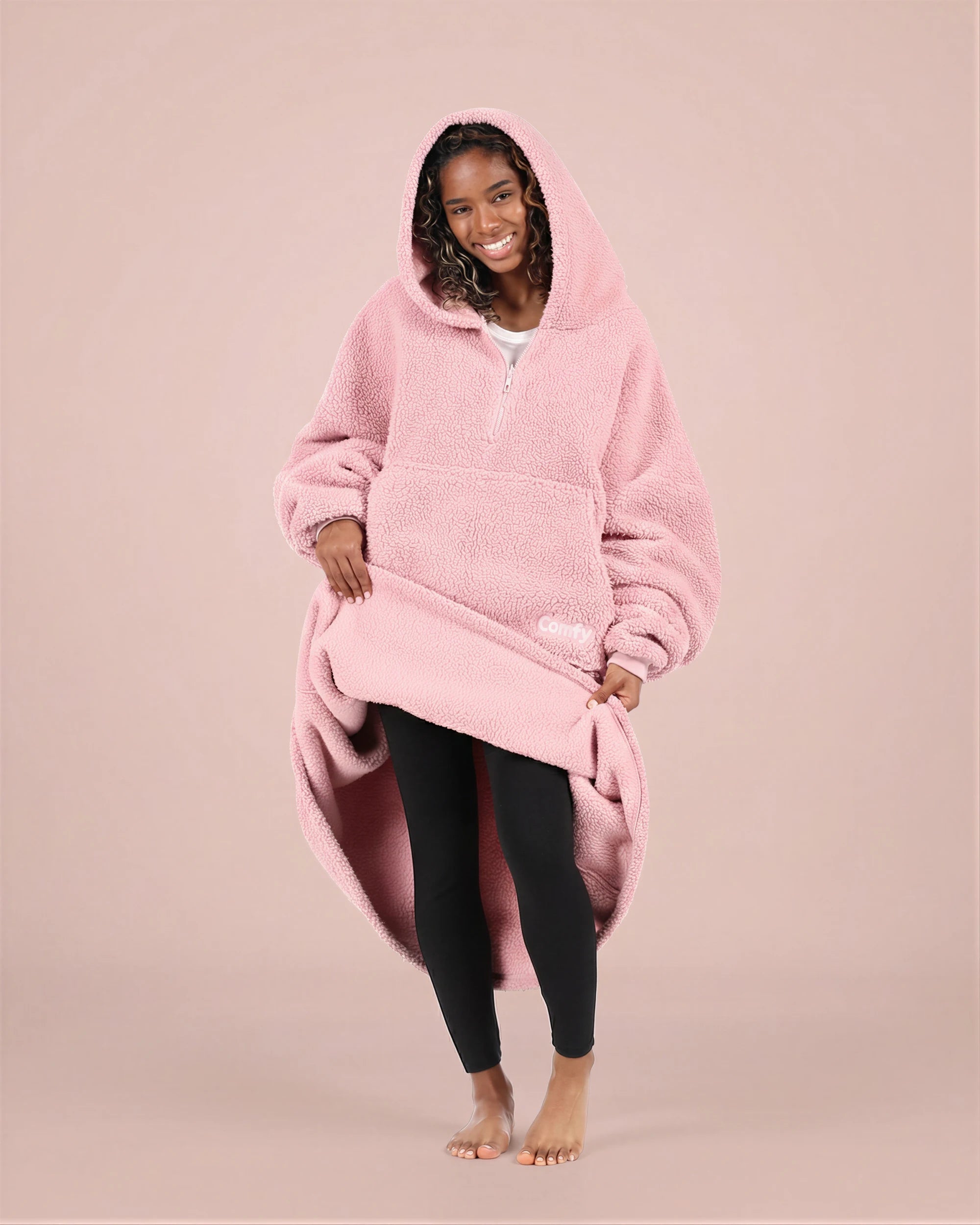 Front view of The Teddy Bear Quarter-Zip wearable blanket in blush with model lifting hem to show full coverage and soft interior