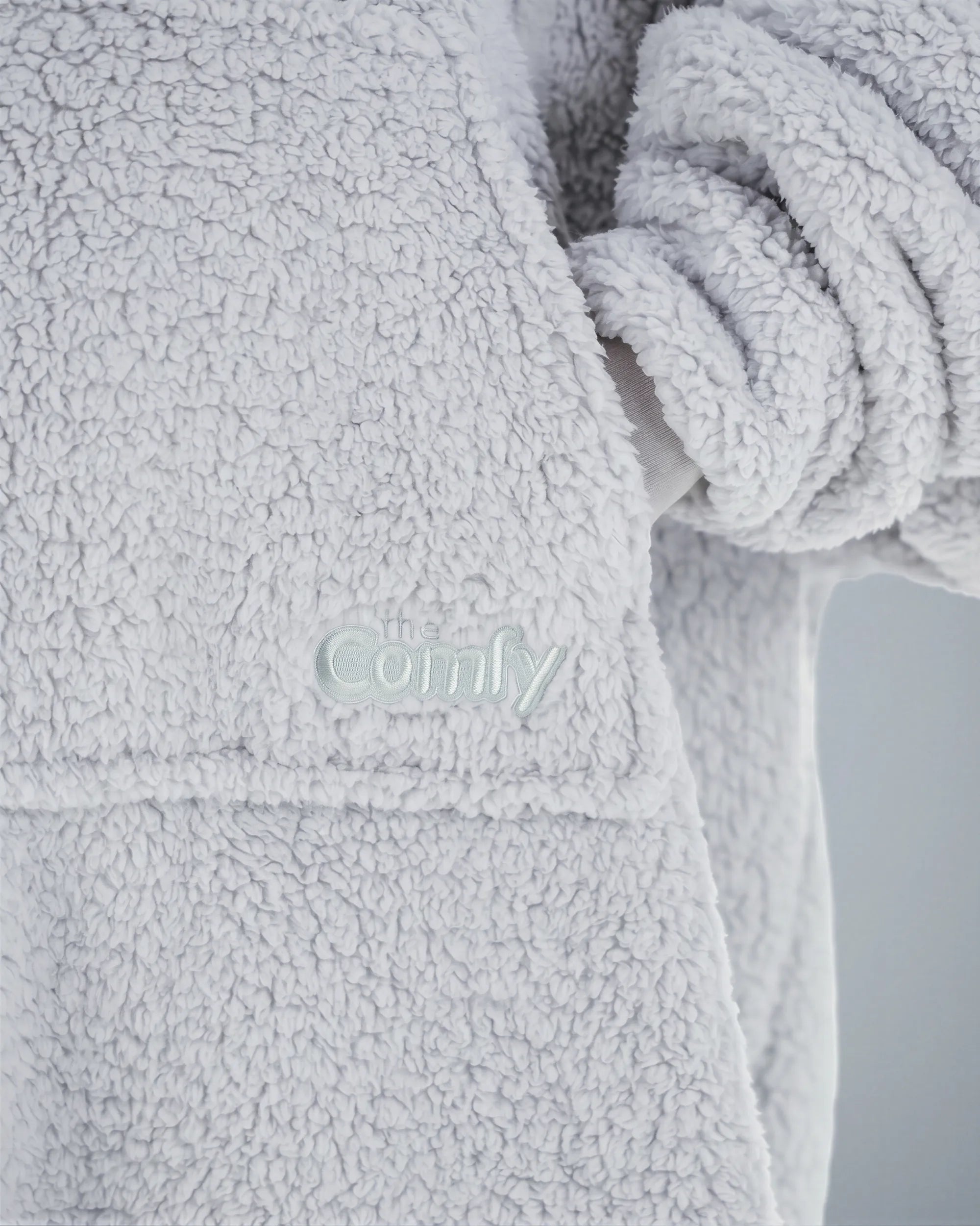 Close-up of The Teddy Bear Quarter-Zip wearable blanket in light gray showing embroidered logo and soft CloudSherpa™ texture