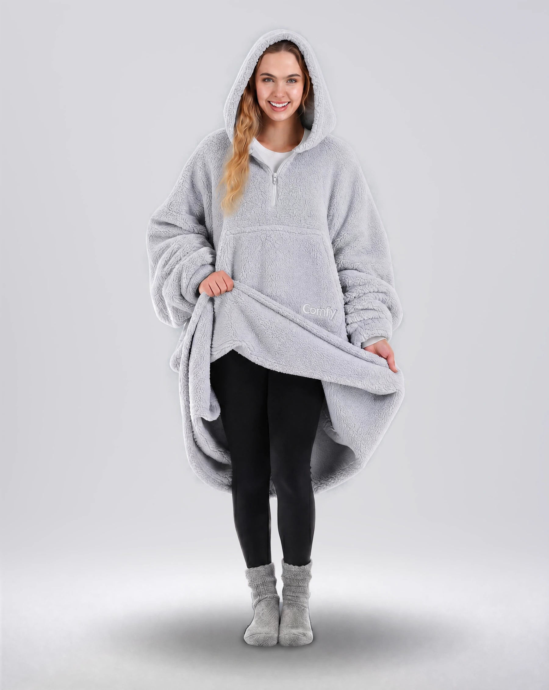 Front view of The Teddy Bear Quarter-Zip wearable blanket in light gray with model lifting hem to show full coverage and plush interior