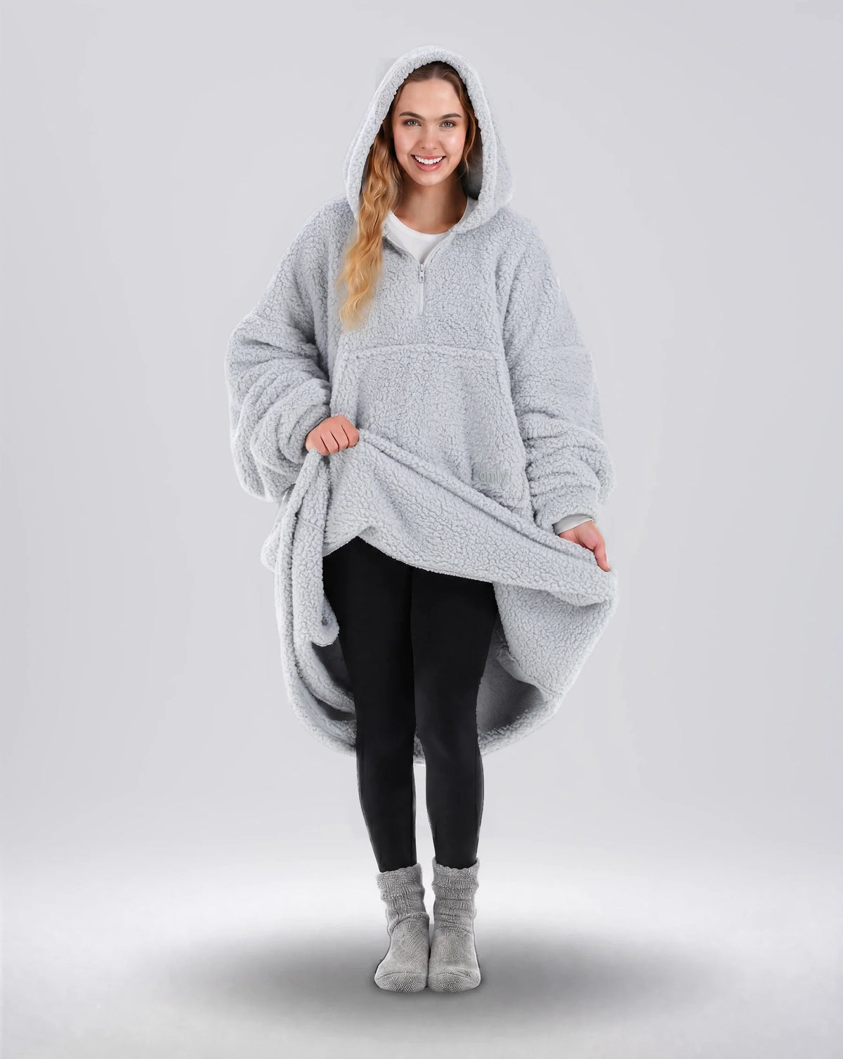 Front view of The Teddy Bear Quarter-Zip wearable blanket in light gray with model lifting hem to show full coverage and plush interior
