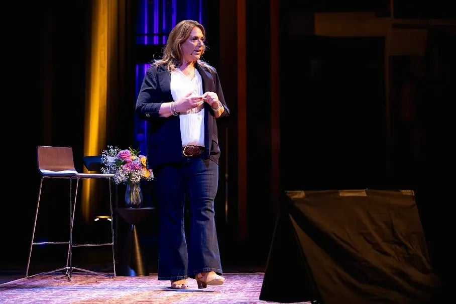 Woman standing on a stage with a microphone, speaking to an audience.