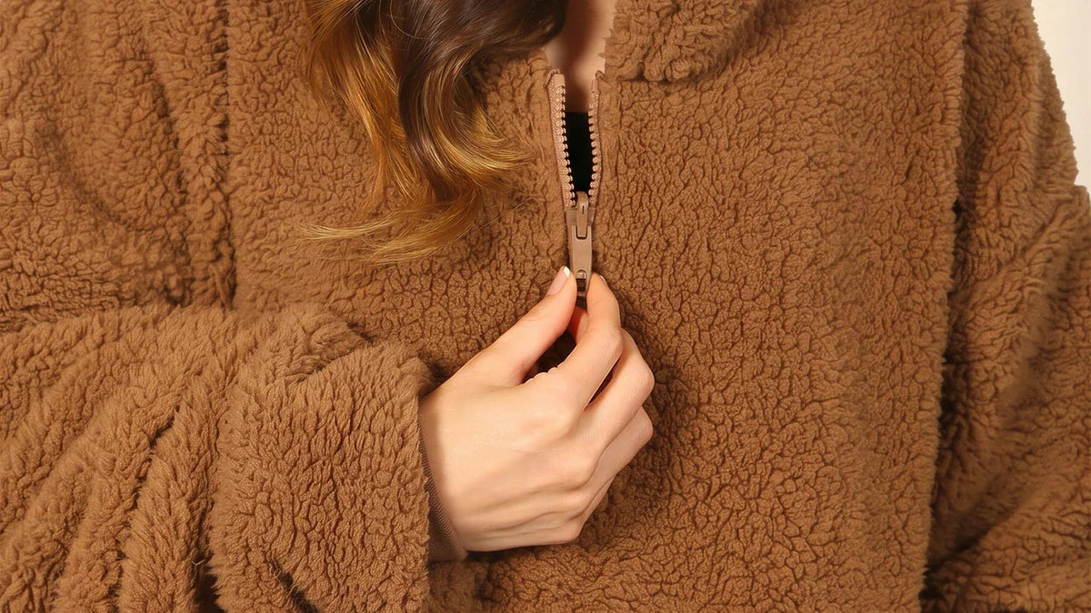 Close-up of the Camel Teddy Bear Quarter-Zip zipper, a hand holding the pull, and the surrounding sherpa texture.