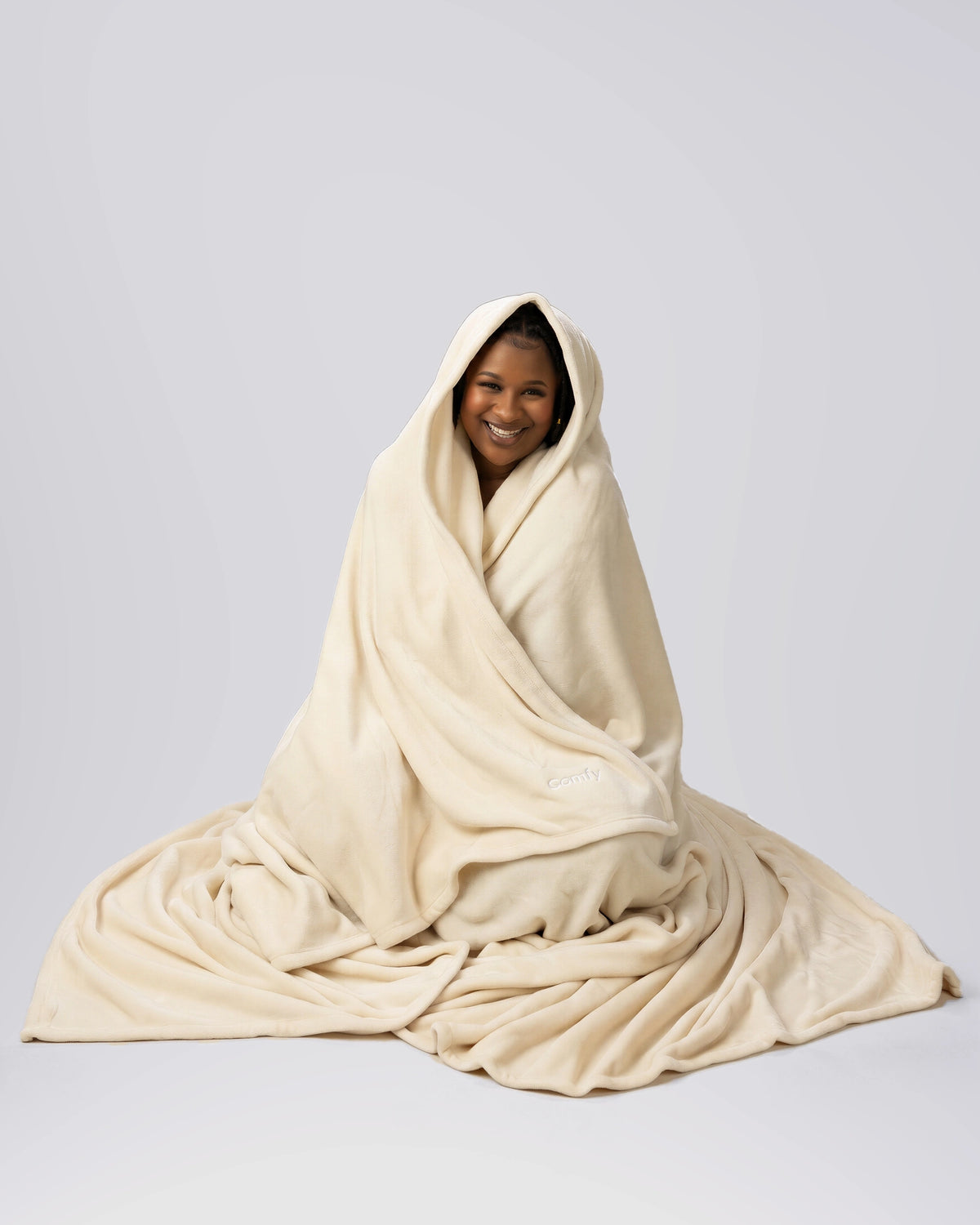 Woman seated while wrapped in The Dream Big Blanket in Cream.