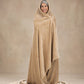 Woman wrapped head-to-toe in a tan oversized blanket, standing against a neutral beige studio backdrop.
