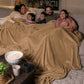 Family of five relaxing together on a sectional sofa under a tan oversized blanket during a cozy movie night.