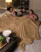 Family of five relaxing together on a sectional sofa under a tan oversized blanket during a cozy movie night.