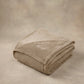 Folded tan oversized blanket with embroidered logo displayed on a matching neutral backdrop.
