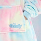 Close-up of the pastel tie-dye wearable blanket fabric, featuring the front pocket and embroidered The Comfy logo.