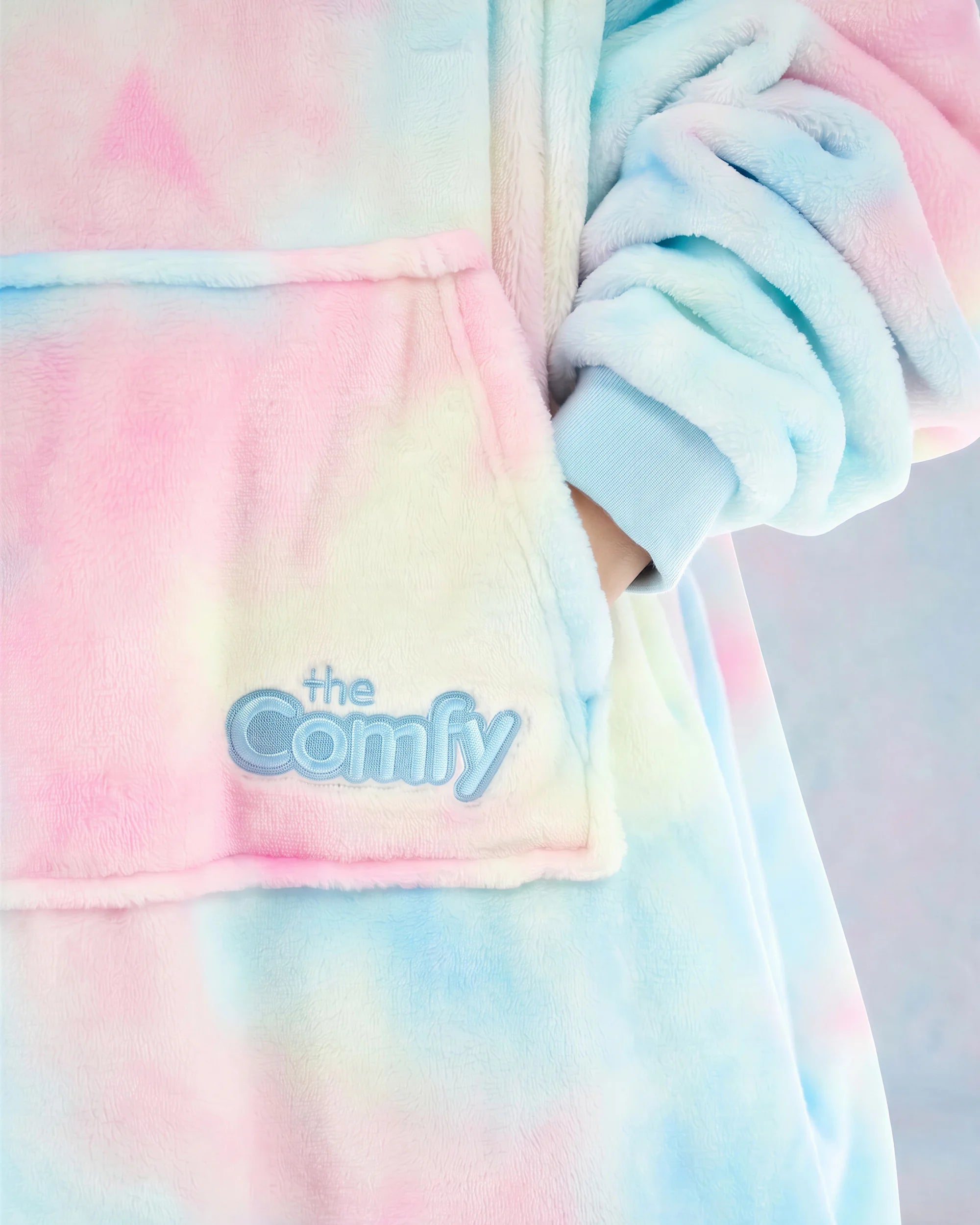 Close-up of the pastel tie-dye wearable blanket fabric, featuring the front pocket and embroidered The Comfy logo.