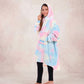 Girl standing in profile wearing a pastel tie-dye wearable blanket with a hood against a neutral studio backdrop.