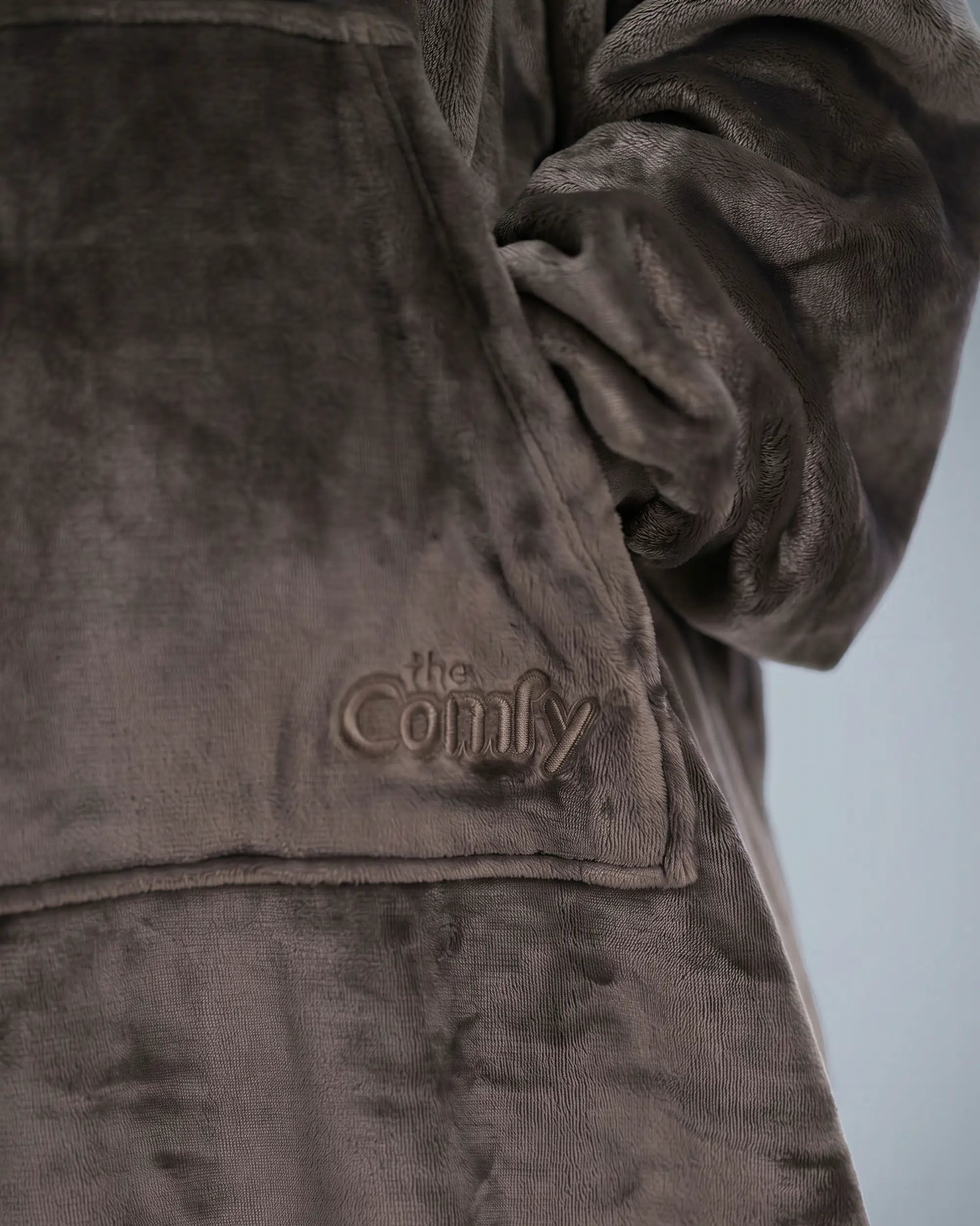 Close-up detail of The Dream Long fabric featuring the ultra-soft microfiber texture, kangaroo pocket construction, and tonal embroidered The Comfy logo.