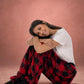Woman sitting with knees hugged while wearing Dream Pants in Red Plaid, showcasing the cozy fit and soft plaid fabric.