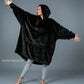 Model wearing The Dream wearable blanket in Black, showcasing the oversized silhouette, hood, and lightweight DreamHaven™ single-layer softness designed for year-round comfort.