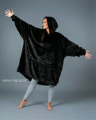 Model wearing The Dream wearable blanket in Black, showcasing the oversized silhouette, hood, and lightweight DreamHaven™ single-layer softness designed for year-round comfort.