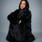 Model wrapped in The Dream wearable blanket in Black, highlighting the cozy oversized fit and relaxed comfort perfect for unwinding at home.