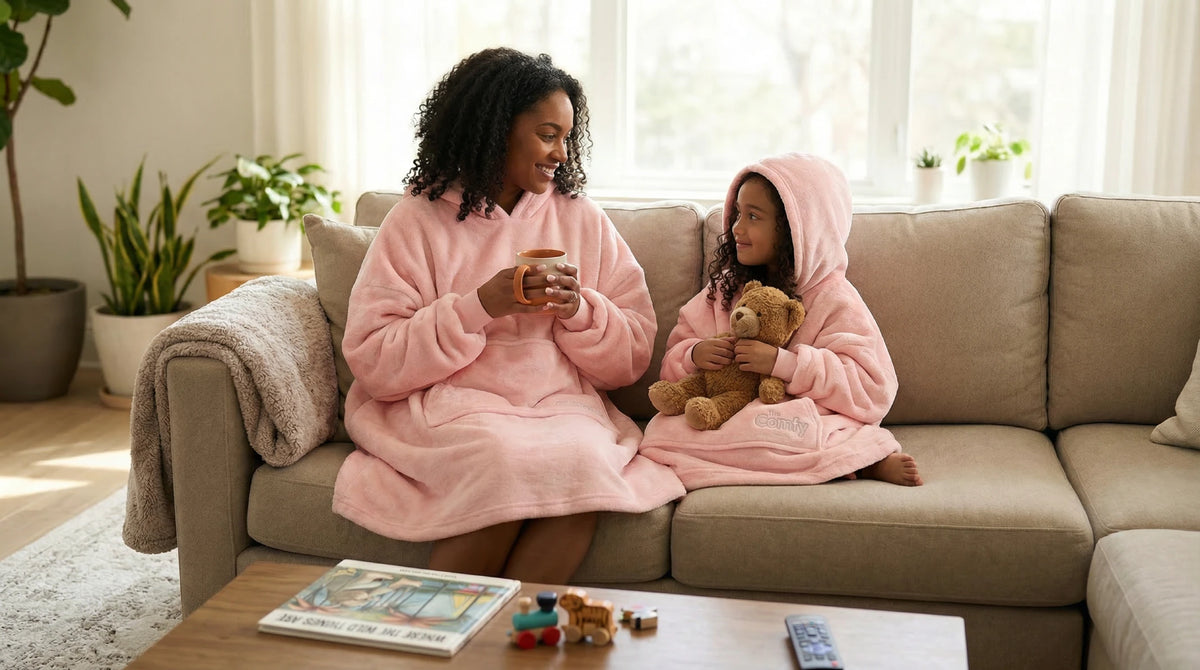 A couple relaxing together on a sofa in burgundy and dark gray Dream wearable blankets.