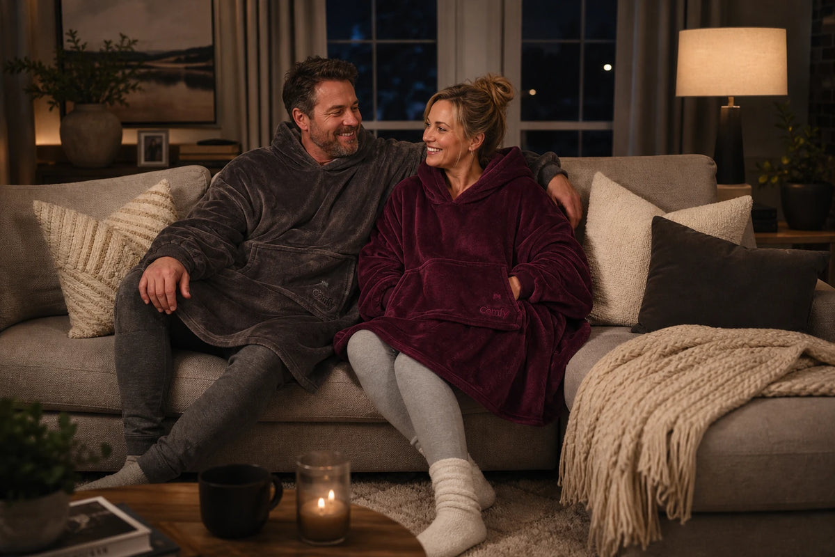 A couple relaxes together on a sofa in burgundy and dark gray Dream wearable blankets.
