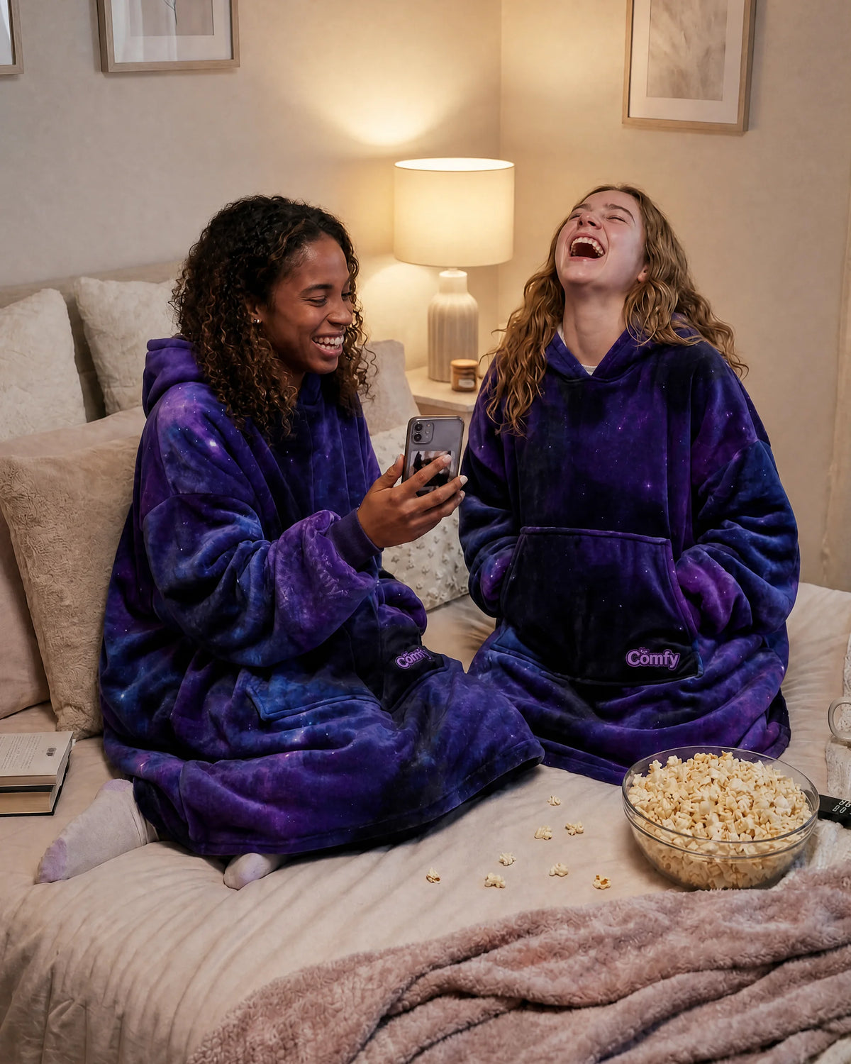 Two friends laugh together in Galaxy Dream wearable blankets during a cozy night in.