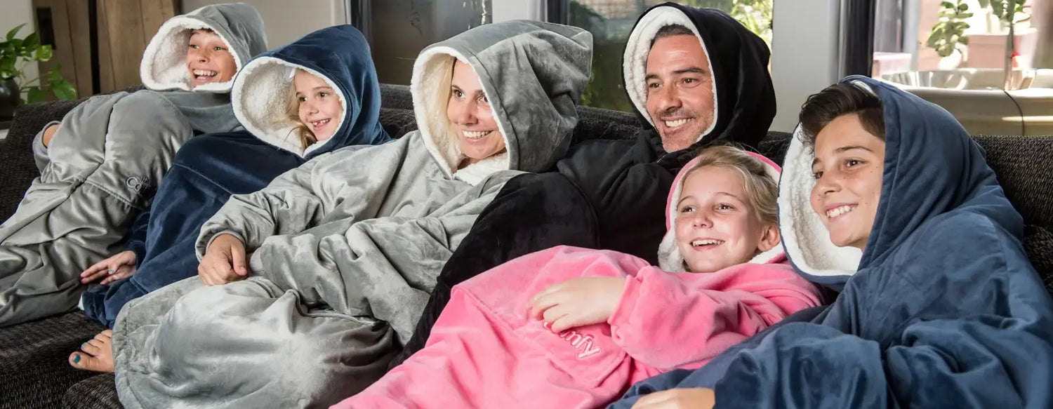 Family of four kids and two parents all wearing the different The Comfy wearable blankets and smiling