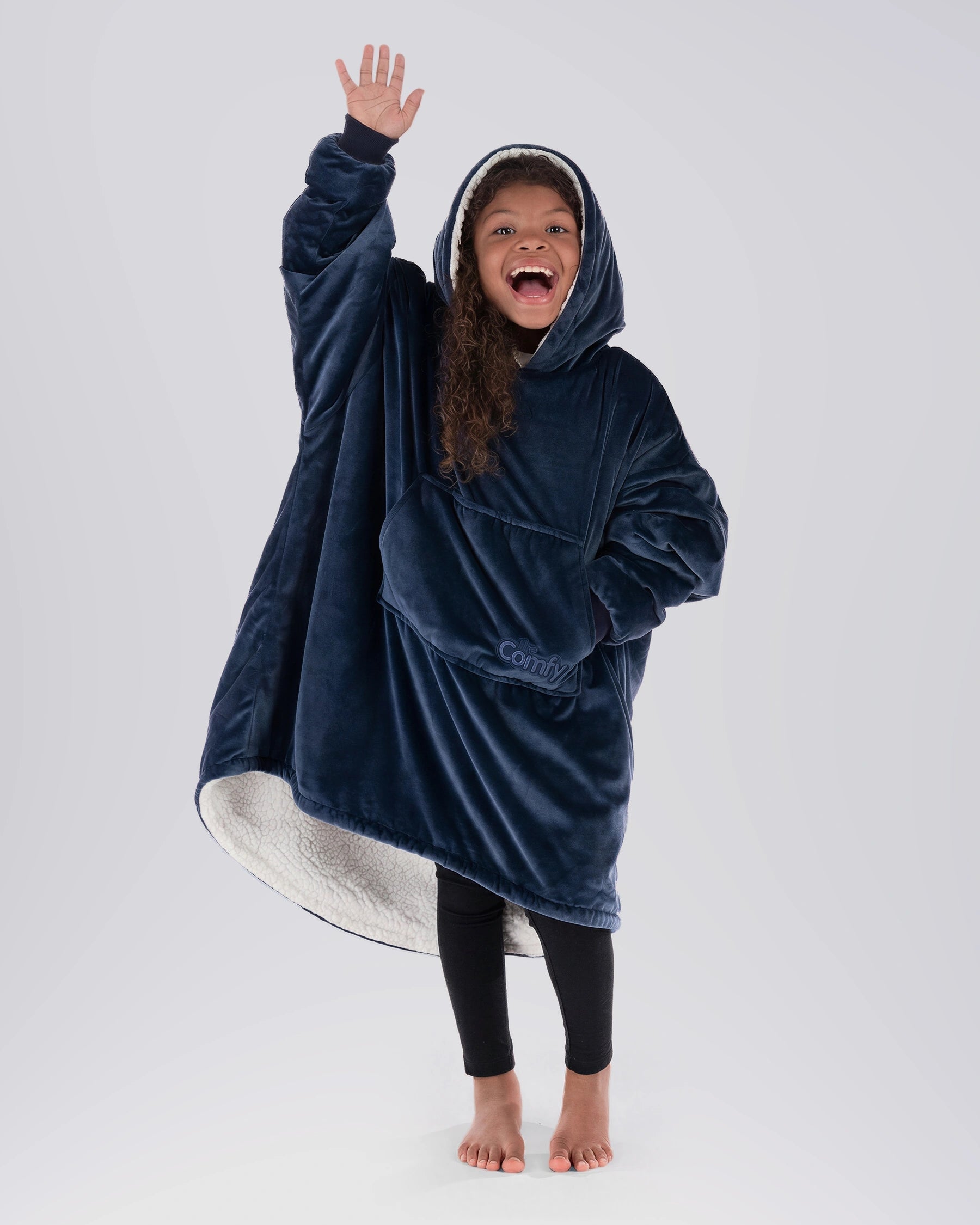 Child wearing The Original Jr. wearable blanket in Blue with CloudSherpa™ lining, waving and showing the oversized fit designed for cozy comfort.