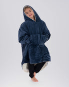 Child wearing The Original Jr. Blue wearable blanket in a relaxed pose, featuring the oversized kangaroo pocket and CloudSherpa™ lining.