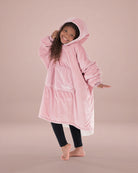 Child wearing The Original Jr. Blush wearable blanket in a playful pose, highlighting the oversized fit and soft hood.