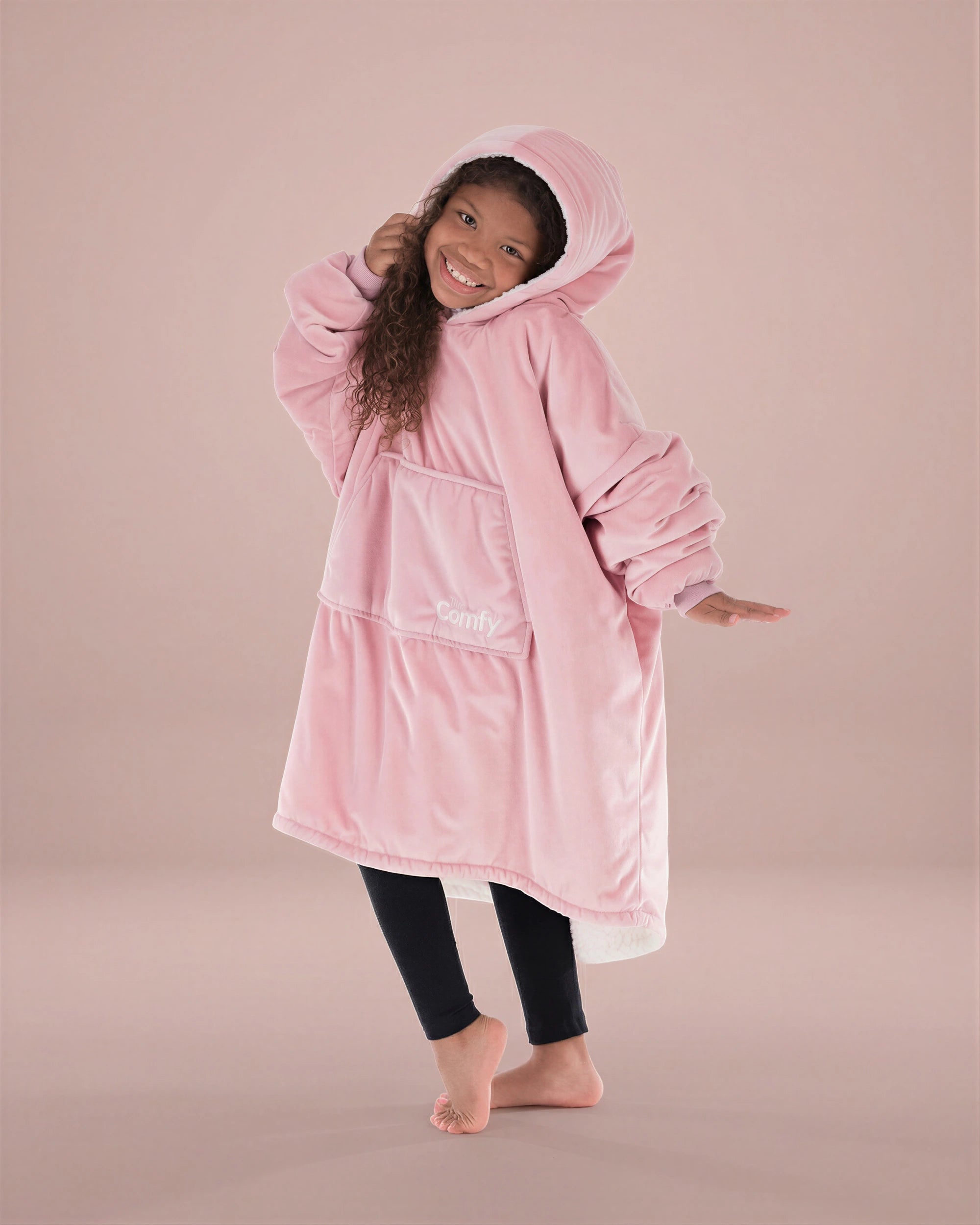 Child wearing The Original Jr. Blush wearable blanket in a playful pose, highlighting the oversized fit and soft hood.