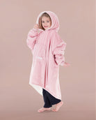 Child wearing The Original Jr. Blush wearable blanket with hood up, featuring the oversized silhouette and front kangaroo pocket.