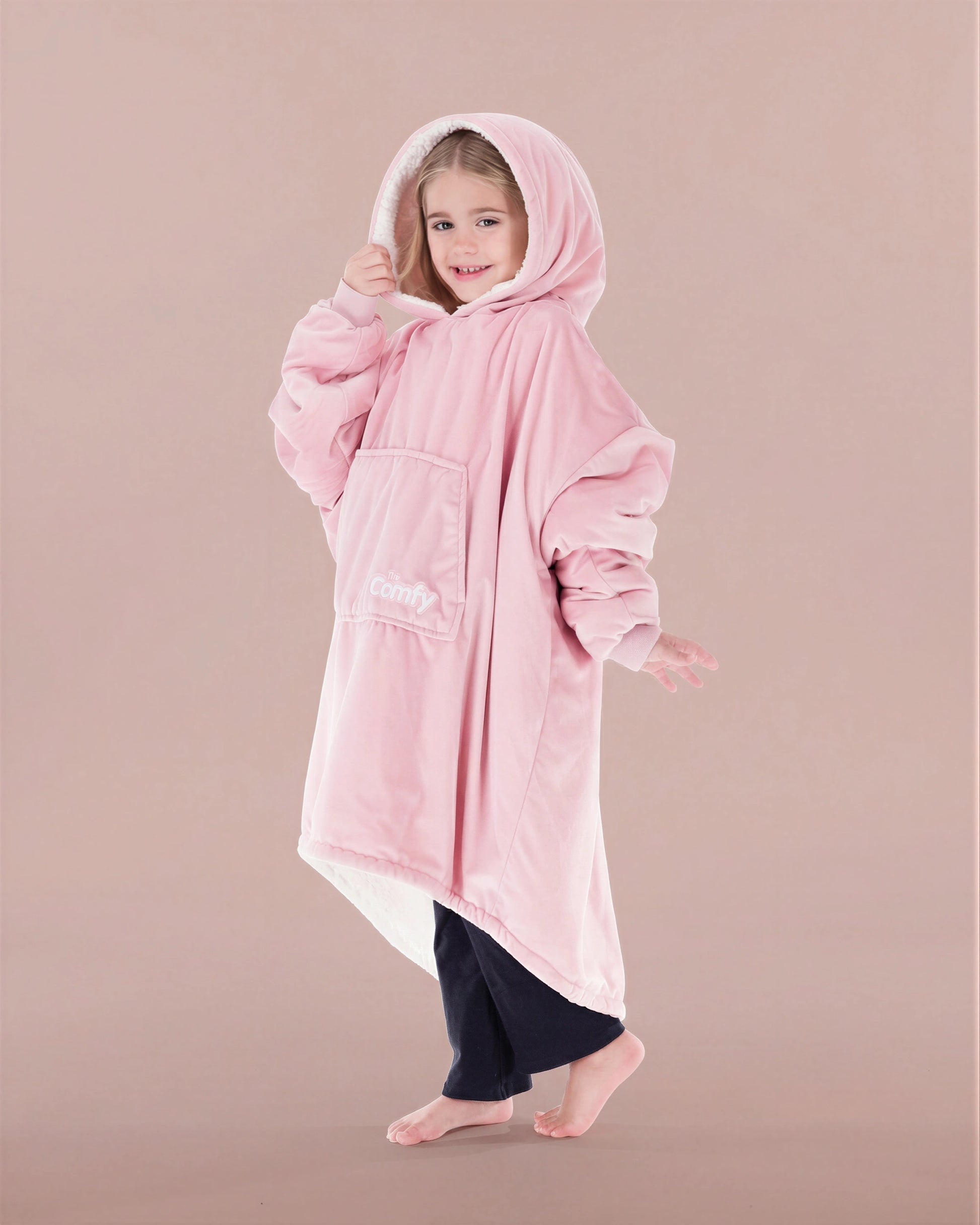 Child wearing The Original Jr. Blush wearable blanket with hood up, featuring the oversized silhouette and front kangaroo pocket.