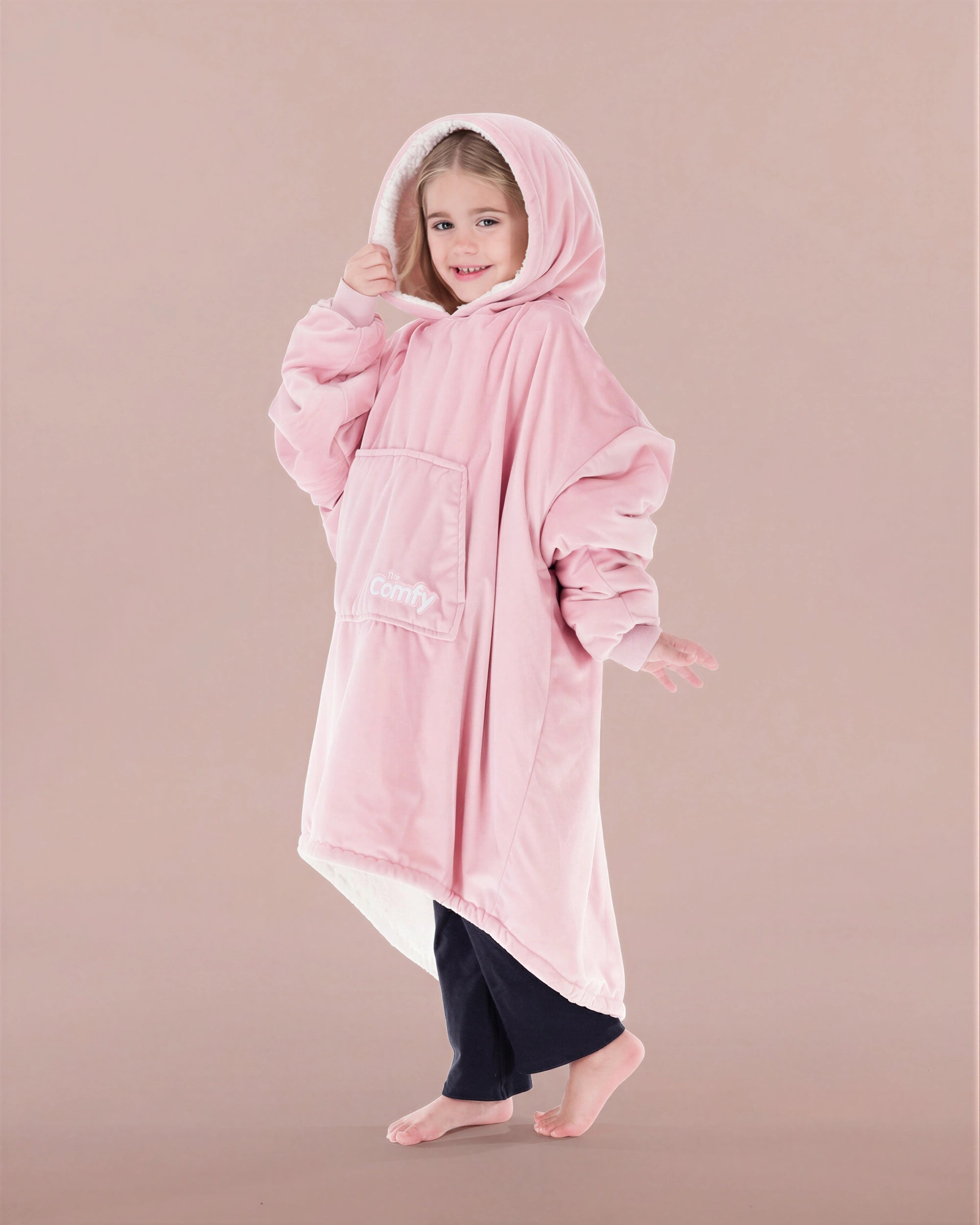 Child wearing The Original Jr. Blush wearable blanket with hood up, featuring the oversized silhouette and front kangaroo pocket.