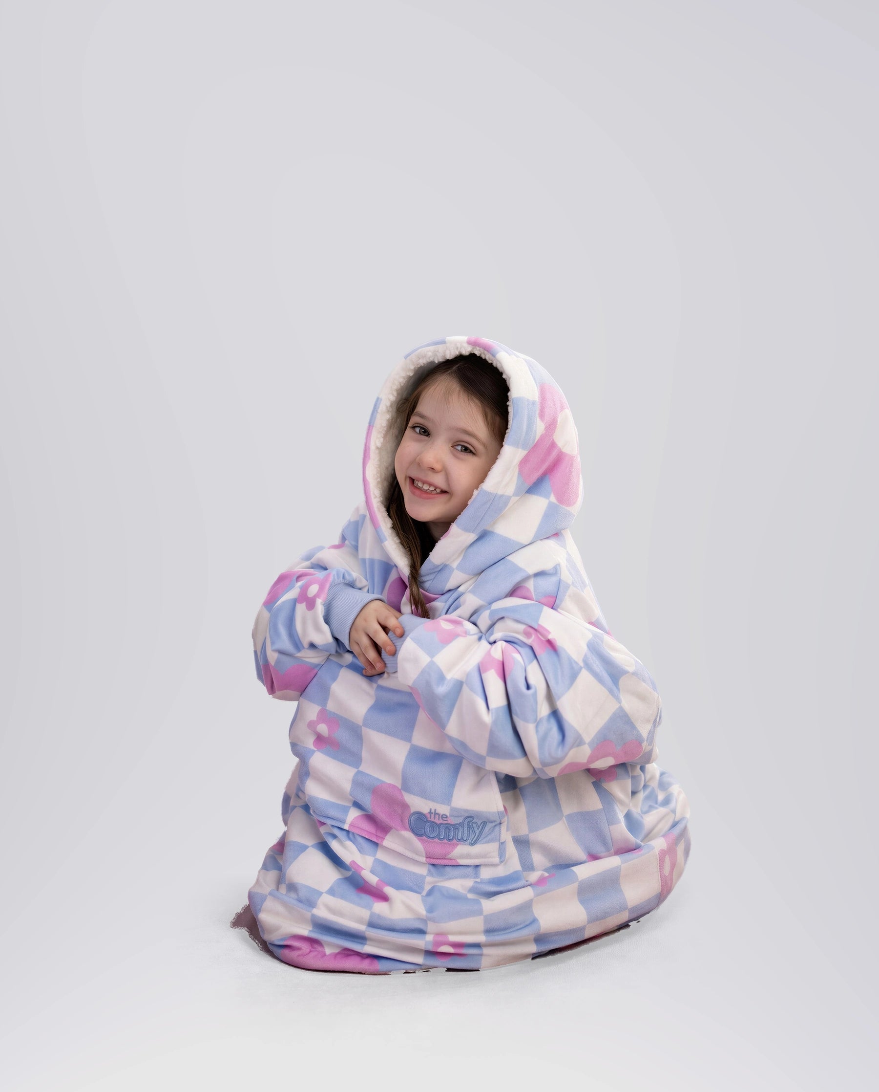 Child sitting comfortably in The Original Jr. Flower Checkered wearable blanket, highlighting full-body warmth and cozy coverage.