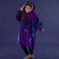 Child wearing The Original Jr. Galaxy wearable blanket in a playful pose, highlighting the oversized hood, kangaroo pocket, and cozy comfort.