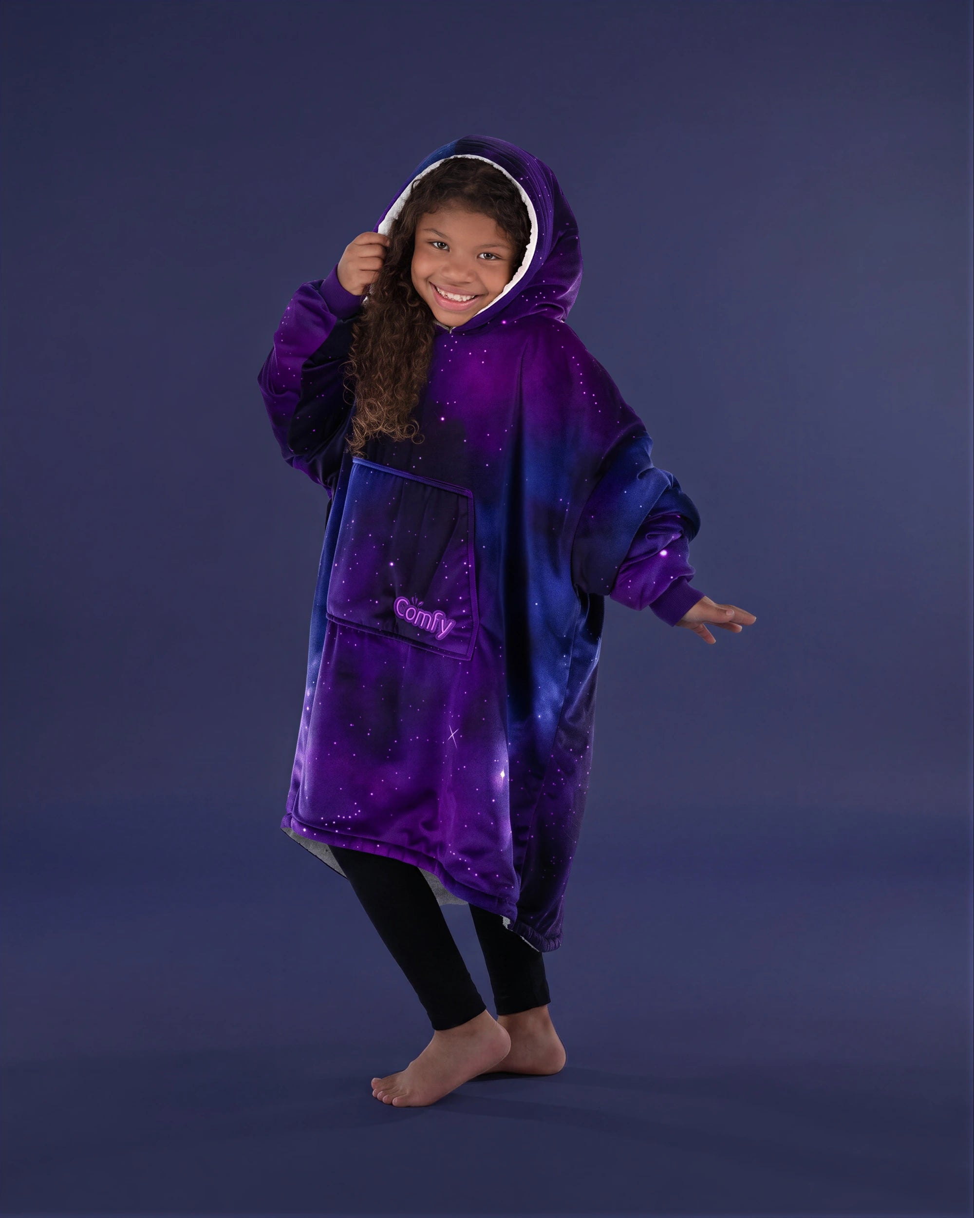 Child wearing The Original Jr. Galaxy wearable blanket in a playful pose, highlighting the oversized hood, kangaroo pocket, and cozy comfort.