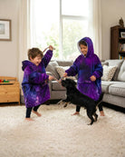 Two children playing indoors with a dog while wearing The Original Jr. Galaxy wearable blankets, designed for comfort during playtime, movie nights, and relaxing at home.
