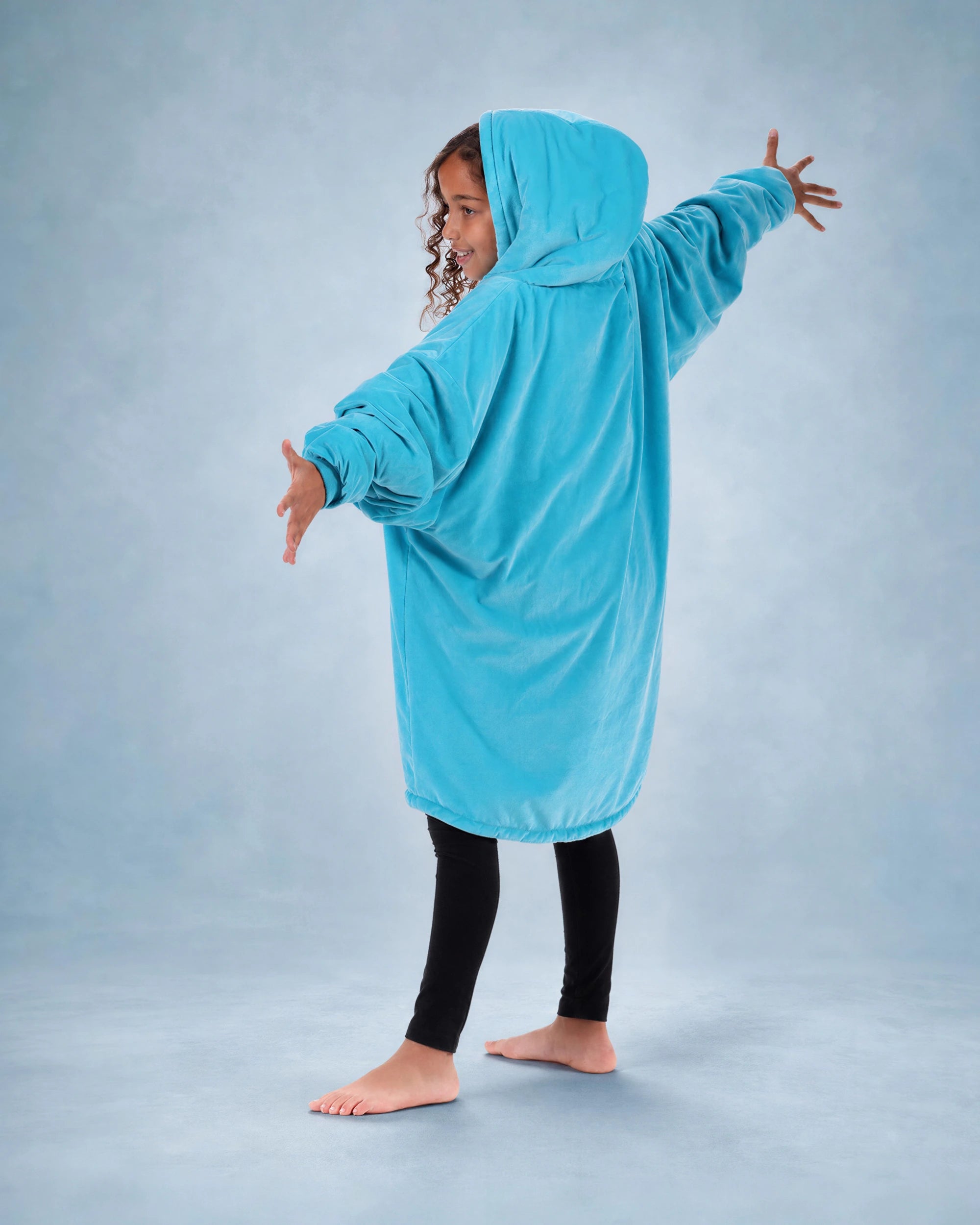 Child wearing The Original Jr. Neon Aqua wearable blanket with arms outstretched, showcasing the roomy silhouette and full-body comfort.