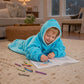 Child relaxing on the floor and coloring while wearing The Original Jr. Neon Aqua wearable blanket, perfect for cozy mornings, quiet activities, and comfort at home.