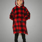Child standing in The Original Jr. Red Plaid wearable blanket, highlighting the oversized fit, roomy kangaroo pocket, and full-body warmth.