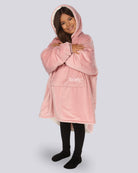 Child wearing The Original Jr. Blush wearable blanket in a hugging pose, highlighting the oversized fit and soft hood.