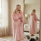 Woman wearing The Comfy Original Long in blush in a cozy bedroom, standing beside a mirror with her dog.
