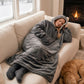 Woman resting on a couch wearing The Comfy Original Long in charcoal beside a fireplace with a sleeping dog.