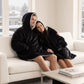 Couple wearing The Original wearable blankets in black relaxing together on a couch in a living room