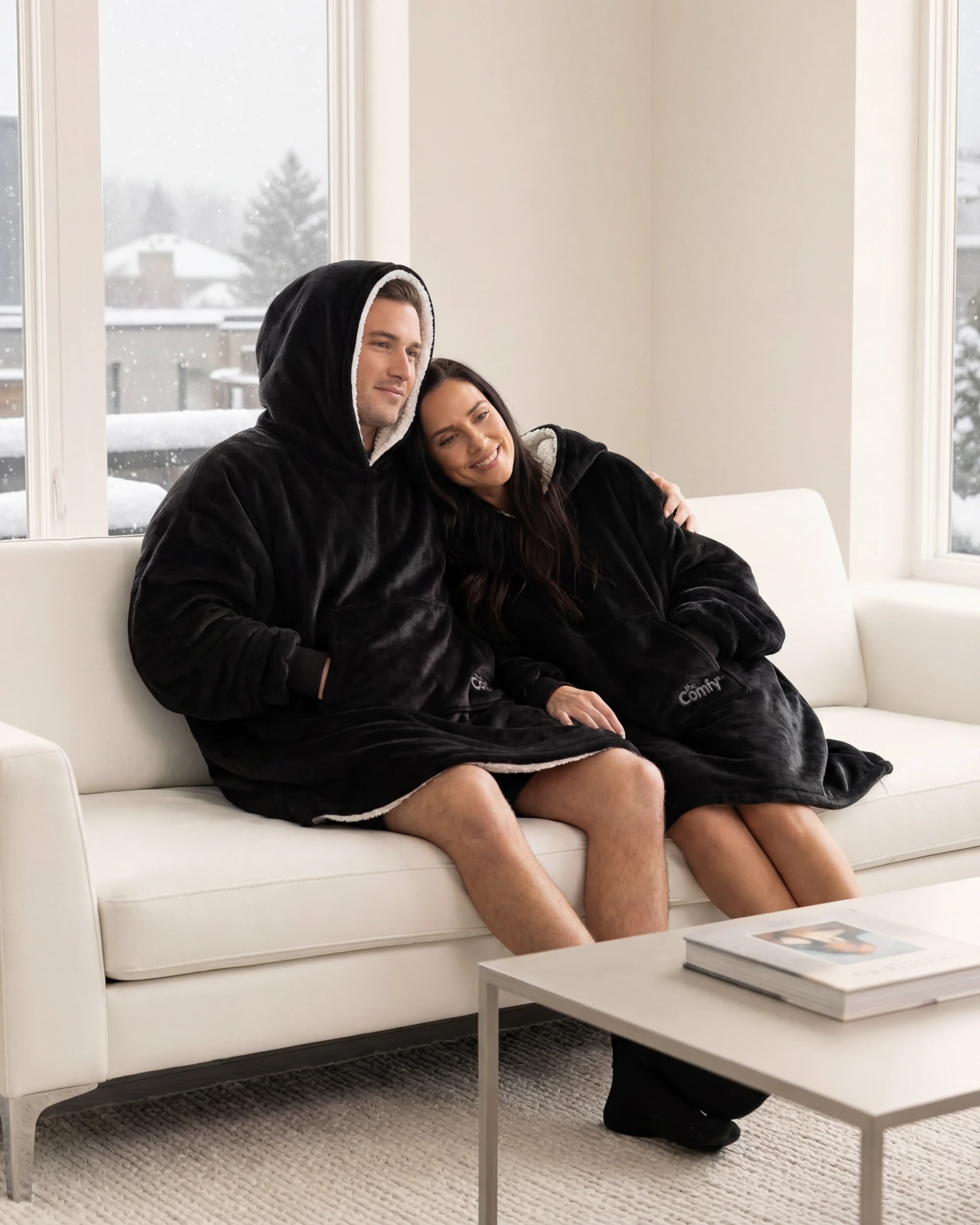 Couple wearing The Original wearable blankets in black relaxing together on a couch in a living room
