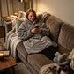 Woman wearing The Original wearable blanket in gray relaxing on a couch while using a phone with a cat nearby