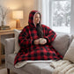 Woman wearing The Original wearable blanket in red plaid sitting on a couch holding a mug while watching snowfall outside