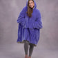 Front-facing lifestyle image of a model wrapped in The Original in Very Perri Purple, emphasizing the oversized fit, plush CloudSherpa™ lining, and cozy hands-in-pocket comfort.