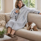 Woman relaxing on a couch in the Teddy Bear Full-Zip worn on the Light Gray side, enjoying cozy comfort with a warm drink and a quiet moment at home.